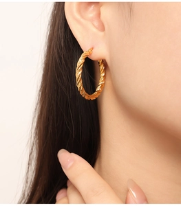 Gros plan de boucles d'oreilles créoles torsadées en or 18 carats portées par un mannequin
