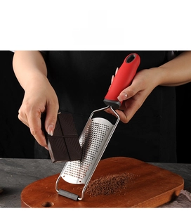 Handheld stainless steel grater with red non-slip handle grating dark chocolate