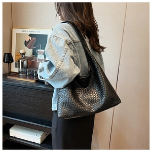 Detail of a black woven leather tote bag with large capacity and thick shoulder strap