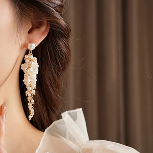 Detail of floral earrings with white pearls and golden tassels worn by a model