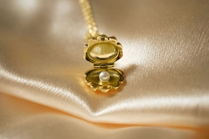 Macro shot of gold shell locket opening to reveal a white pearl on satin fabric