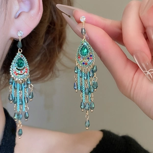 Close-up of green crystal water drop earrings with golden chain tassels in boho style