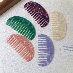 Five colorful marble pattern acetate wide-tooth combs for hair styling on white fabric