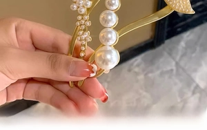 Detail of elegant gold-toned hair clip featuring delicate white pearls and floral metal clusters