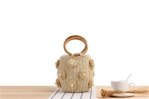 Detail of straw bucket bag featuring woven flowers, pearls and round handles