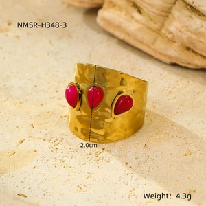 Macro view of wide gold ring with pleated texture and three red teardrop gemstones