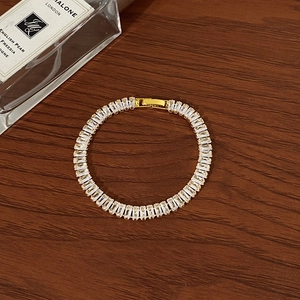 Macro detail of gold baguette-cut zircon tennis bracelet on dark wood background