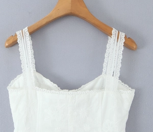 Detail of white floral lace top with embroidery on a wooden hanger against a grey wall