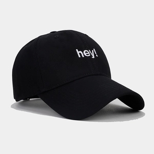 Detailed close-up of white 'hey!' embroidery on a black cotton twill baseball cap