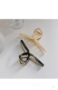 Close-up of elegant large metal hair claws in beige and black with twisted cross design