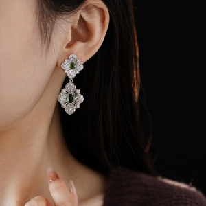 Close-up of vintage silver earrings with green stones and zircons worn on model