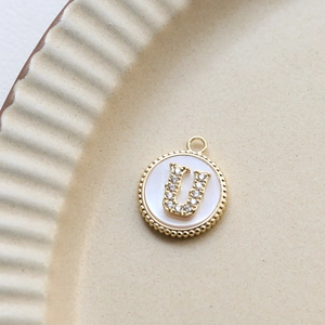 Detailed view of a gold-plated letter U pendant with cubic zirconia and shell inlay