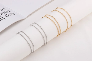 Detailed view of gold and silver stainless steel beaded curb chains on a white pedestal
