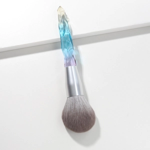 Macro detail of large powder brush with icy blue gradient crystal handle and soft grey bristles