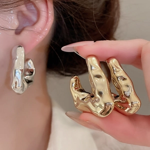 Detailed view of C-shaped earrings with liquid metal lava texture in gold and silver