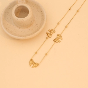 Golden bowknot necklace in stainless steel shown on a beige minimalist background