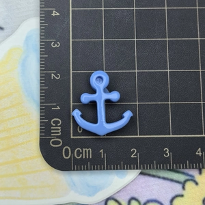 Macro shot of a light blue anchor charm next to a ruler showing its 2cm small size