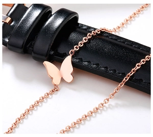 Macro shot of rose gold butterfly pendant on fine link chain over black leather