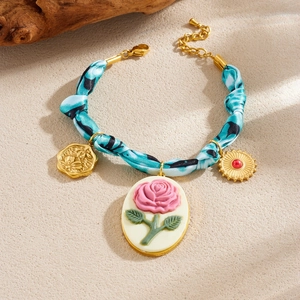 Blue fabric and gold chain necklace set with carved rose and coin charms on beige background