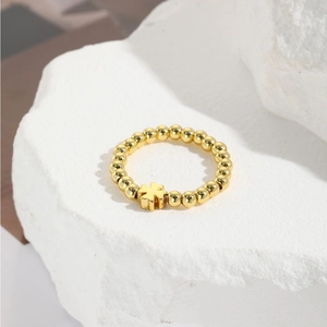 Golden handmade elastic beaded ring with a cross pendant on a minimalist background