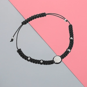 Macro shot of Saint Benedict Medal charm on black woven adjustable rope bracelet