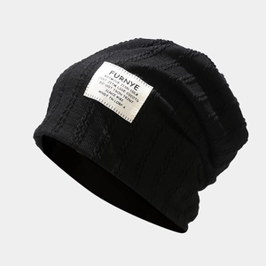 Detail of black cable knit beanie featuring a white rectangular stitched fabric logo label