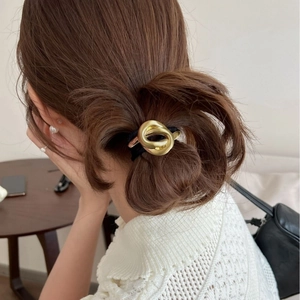 Detail of a minimalist gold metal knot hair tie worn on hair in a home setting