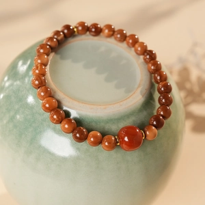 Close-up of red agate beaded bracelet with gold spacers on a ceramic jar lid