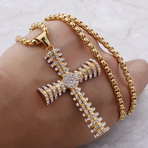 Close-up of hand holding a gold cross pendant with cubic zirconia on a box chain