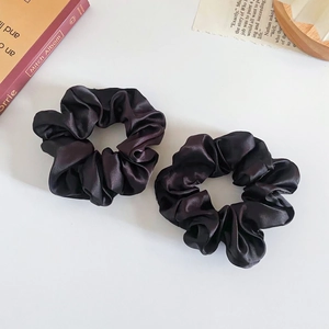 Close-up of two black silk satin hair scrunchies on a white desk with aesthetic book props