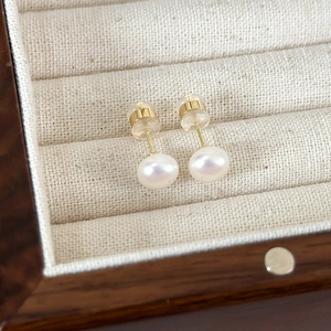 Detail of cream white pearl earrings with gold posts on a beige jewelry display tray