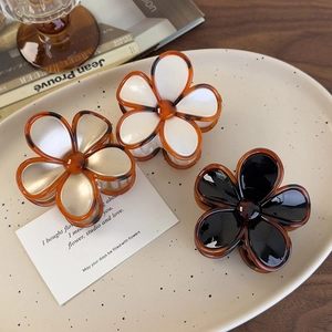 Three elegant vintage floral hair claws in amber, black, and white on a lifestyle platter