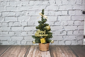 Mini desktop Christmas tree with gold ornaments, bows and Merry Christmas sign on wood
