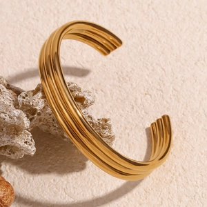 Detailed macro of 18K gold plated triple-layer open bangle on a textured surface