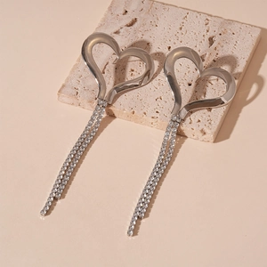 Macro detail of silver heart tassel earrings with sparkling rhinestones on beige stone