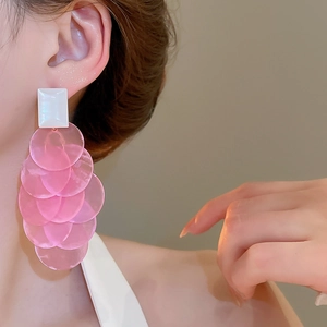 Close-up of long drop earrings featuring layered pink shell-like discs and white studs