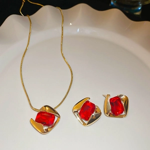 Macro shot of gold geometric necklace and earrings set with rectangle red gemstones