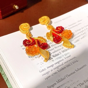 Macro shot of vintage gold earrings with red enamel on an open book page