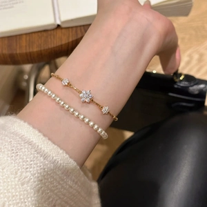 Detail of layered jewelry set featuring white pearl bracelet and golden zircon flower chain