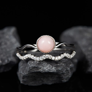 Detail of pink gemstone ring and diamond-studded wavy band on black rock background