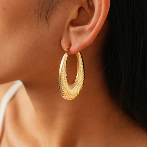 Close-up of chunky gold teardrop earrings with textured ribbed design on model