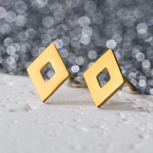 Detailed view of geometric hollow rhombus earrings in gold finish on white texture