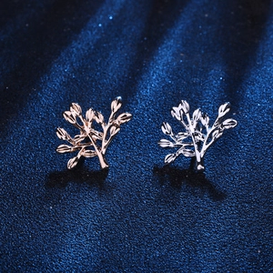 Macro detail of leaf-shaped stud earrings in rose gold and silver on textured background