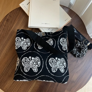 Detailed view of black canvas bag with white butterfly embroidery and metal snap button