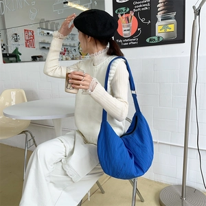 Detail view of royal blue pleated dumpling bag with adjustable strap in a café setting