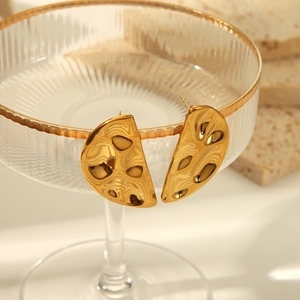 Détail de boucles d'oreilles irrégulières dorées avec texture martelée sur bord de verre