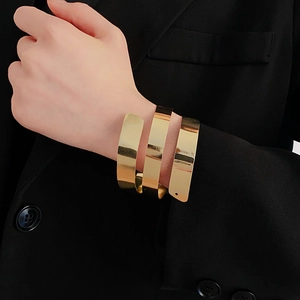 Macro shot of minimalist triple-layer gold spiral cuff bracelet on a black blazer sleeve