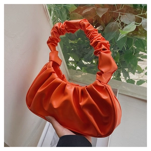 Detail of soft pleated orange cloud bag with textured handle held against a window