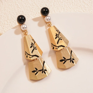 Gold vintage tassel earrings with pearls and black leaf branch pattern on a white plate