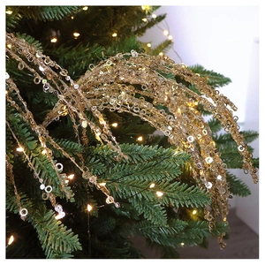 Close-up of golden sequin branches hanging on a green Christmas tree with warm lights